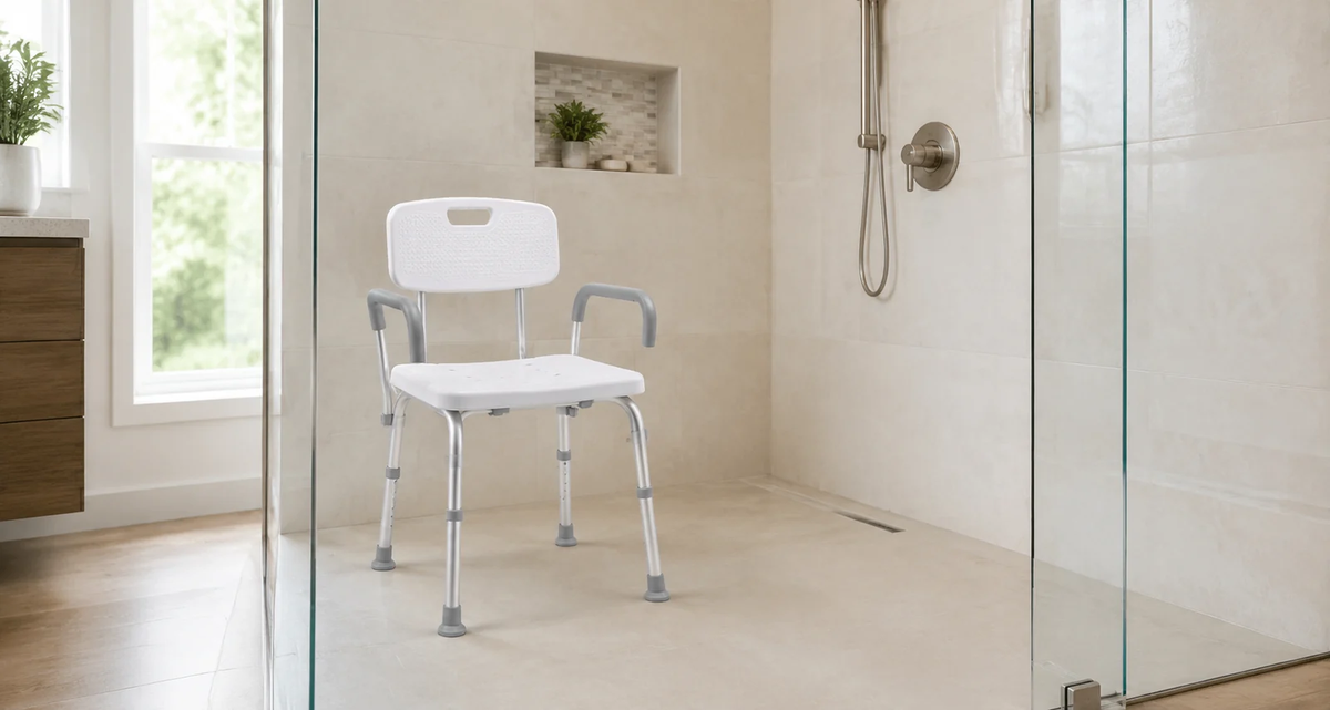 White shower chair with backrest, armrests, and adjustable legs positioned inside a bright walk-in shower.
